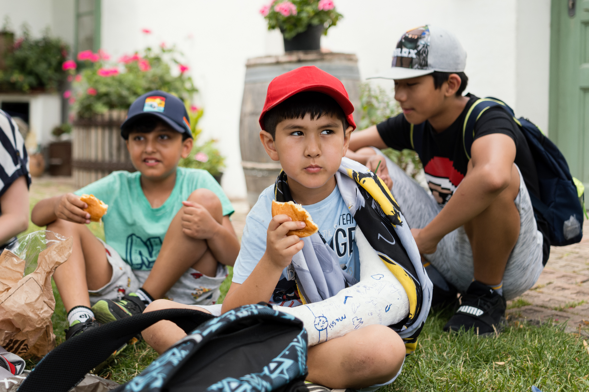 drei Jungs aus dem LernLEO, sitzen auf einer Wiese und machen Pause, alle tragen kurze Hose, T-Shirt und Kapperl als Kopfbedeckung