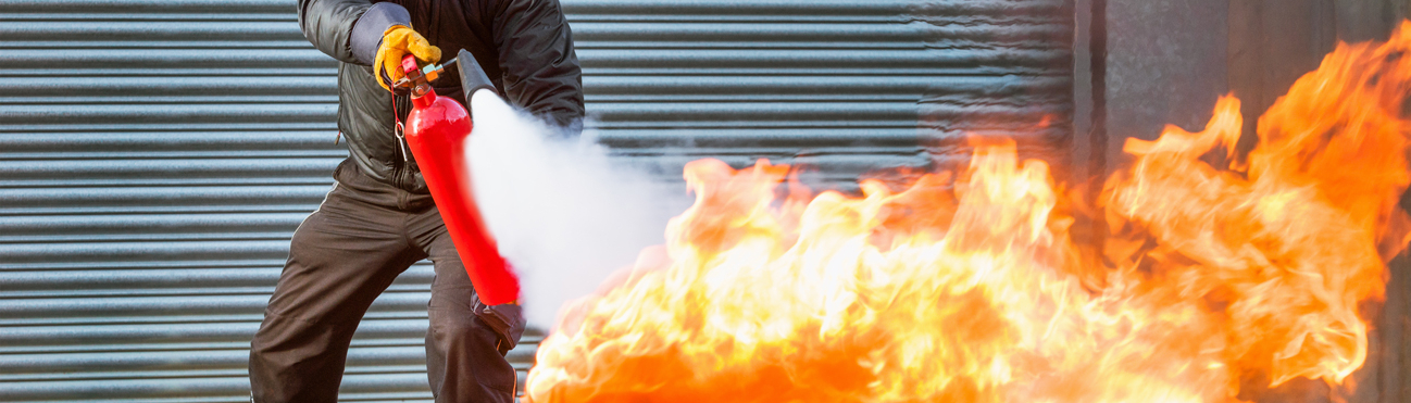 es steht ein Mann vor einer Garage mit einem Feuerlöscher da und er versucht das Feuer in der Tonne zu löschen