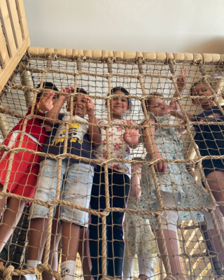 LernLEO Kinder in einem Indoor-Spielplatz, mehrere Kinder hinter Kletterwand, schauen und lachen alle in Kamera