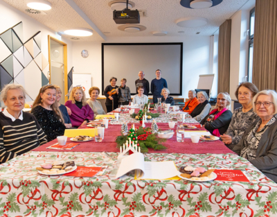 12 ältere Frauen sitzen auf einem langen weihnachtlich gedecktem Tisch, am Ende stehen Mitarbeiterinnen und zwei Mitarbeiter vom Samariterbund