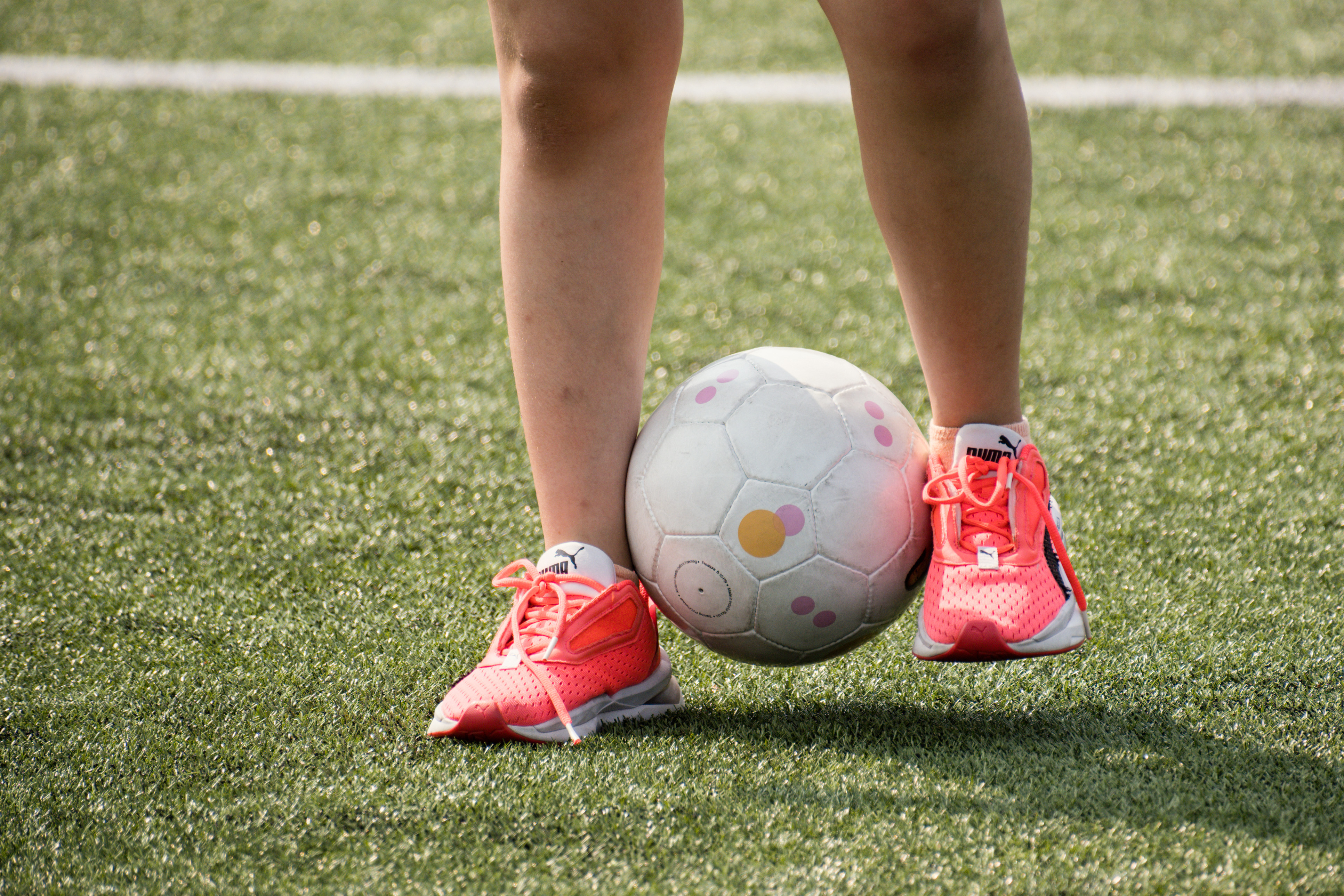 Detailaufnahme von zwei Füßen in rosaroten Schuhen, die einen Fußball zwischen sich haben