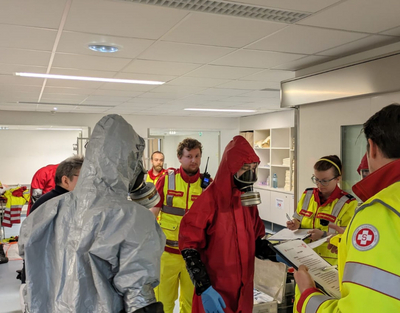 Personen in Schutzanzug und Personen in Sanitäter Uniform haben eine Besprechung.