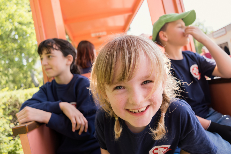 Fröhliche Kinder in einem offenen Zugwagen: im Vordergrund ein lachendes Mädchen mit blonden Haaren, im Hintergrund andere, Kinder die entspannt sitzen 