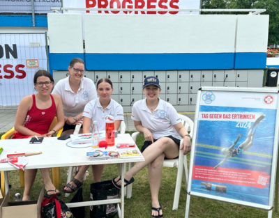 Vier Frauen sitzen an einem Tisch, daneben ein Aufsteller der den Tag gegen des Ertrinken bewirbt.