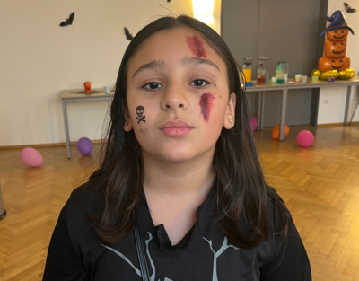 Ein Mädchen mit Halloween Makeup sitzt in einem Raum mit Luftballons und dekorierten Tische.