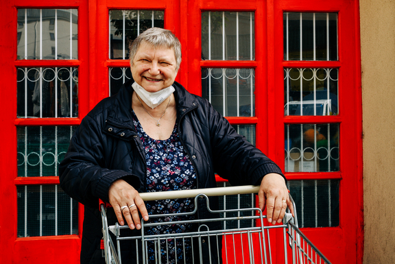 Frau vor roter Türe des Sozialmarktes lehnt an Einkaufswagen