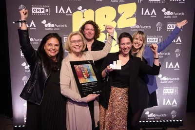 Gruppenfoto fünf Personen stehen freudig vor Fotowand bei den Effie Awards, halten Awards in der Hand und lächeln in Kamera