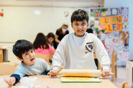 Zwei Kinder backen gemeinsam in einem Klassenraum und lächeln fröhlich.