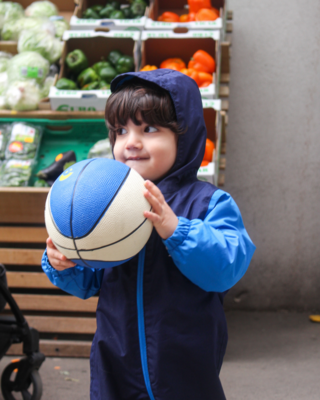 Nahaufnahme kleiner Junge im Sozialmarkt, hält Ball in den Händen und freut sich sichtlich, Jacke mit Kapuze auf Kopf