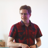 Ein Mann, der ein kariertes Hemd und eine Brille trägt, schaut zur Seite.