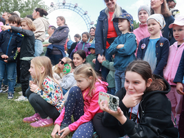 Eine Gruppe von Kindern und Erwachsenen schaut interessiert in eine Richtung. Dahinter Riesenrad im Prater in Wien. 
