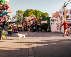 Rettungshundeführerin hat Rettungshund an Leine, gehen über Pratergelände, im Hintergrund Spielbuden und Menschen