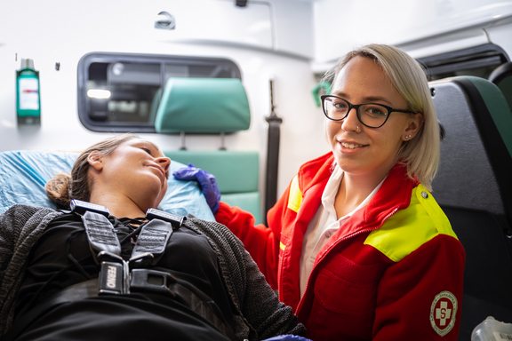 Patientin auf Liege und sitzende Sanitäterin im Einsatzfahrzeug