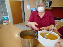Eine Frau serviert Suppe aus einem Topf in eine Schüssel.