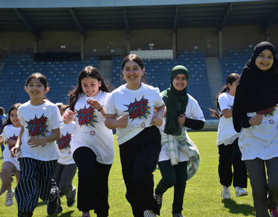 Mehrere Mädchen laufen lachend über ein Fußballfeld und tragen ein PowerLEO T-Shirt.
