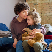 Mutter und Tochter sitzen auf Bett und Mutter legt Arm um Tochter