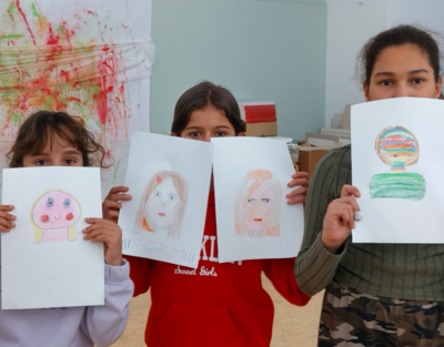 Drei Mädchen halten selbst kreierte Zeichnungen in die Höhe.