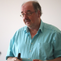 Ein Mann in hellblauem Hemd und mit Brille spricht mit jemanden. 