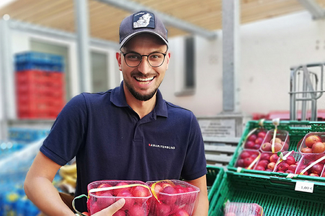 Sozialmarkt Mitarbeiter hält verpackte Pfirsiche und lächelt in Kamera