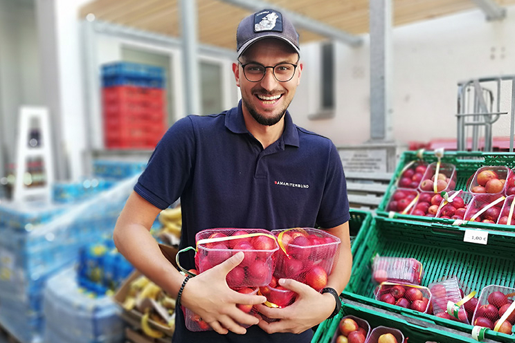 Sozialmarkt - Mitarbeiter hält verpackte Pfirsiche und lächelt in Kamera