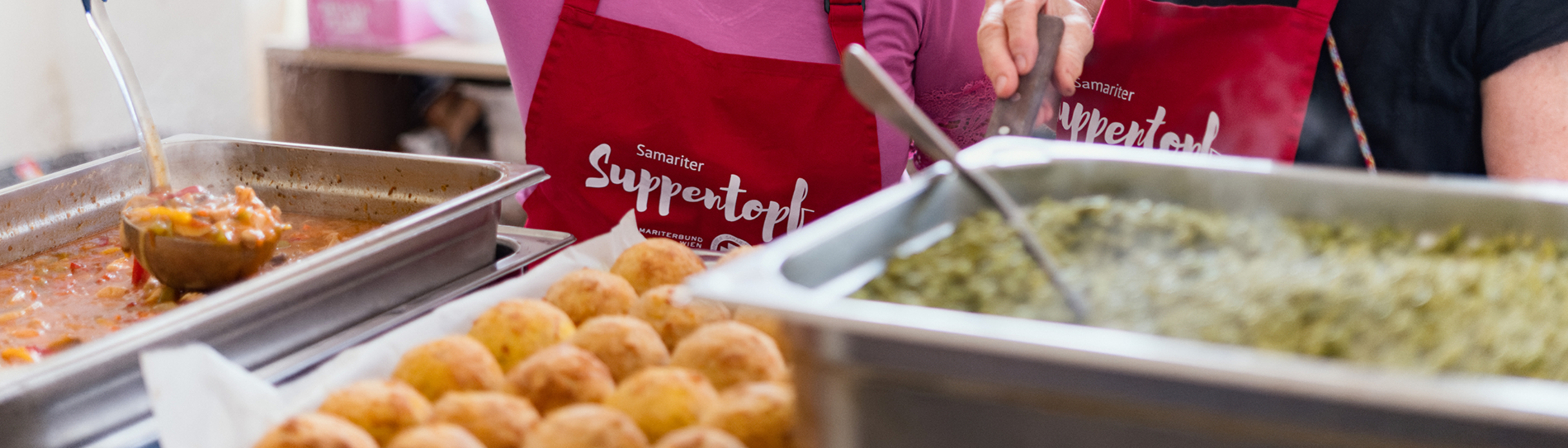 Zwei Frauen in Schürzen, die Essen in einer Küche zubereiten und lächeln.