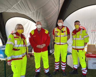 Gruppenbild Sanitäter:innen in Uniformen in einem Einsatzzelt, alle tragen FFP2-Masken