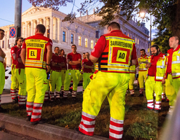 Mehrere Rettungssantitäter:innen stehen in einem Halbkreis und haben eine Besprechung.