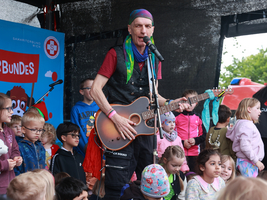 Kinderliedermacher Bernhard Fibich beim Tag des Samariterbundes mit Gitarre unterhält Kinder auf einer Bühne.