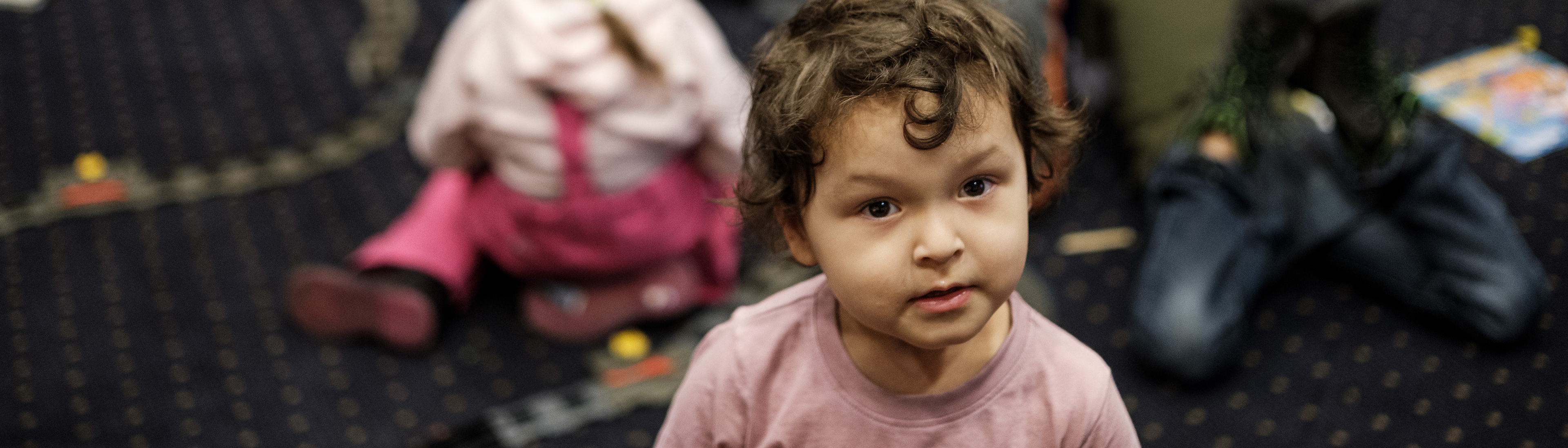 Kleines Mädchen sitzt auf Teppichboden in Flüchtlingseinrichtung und spielt