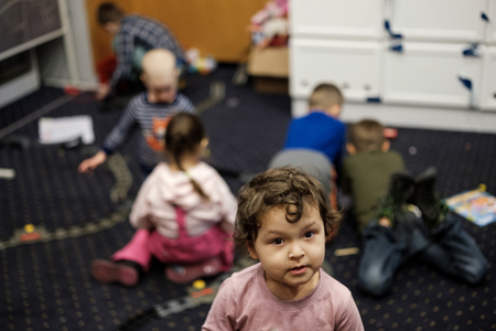 Kleines Mädchen lächelt in Kamera und fünf weitere Kinder spielen im Hintergrund
