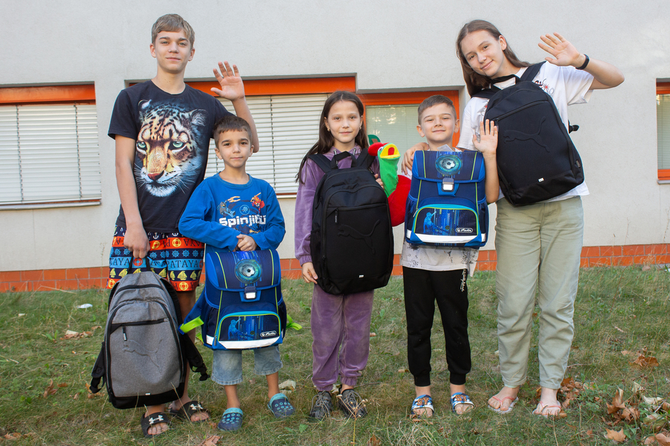 Drei Kinder und zwei Jugendliche freuen sich über ihre neuen Schultaschen 