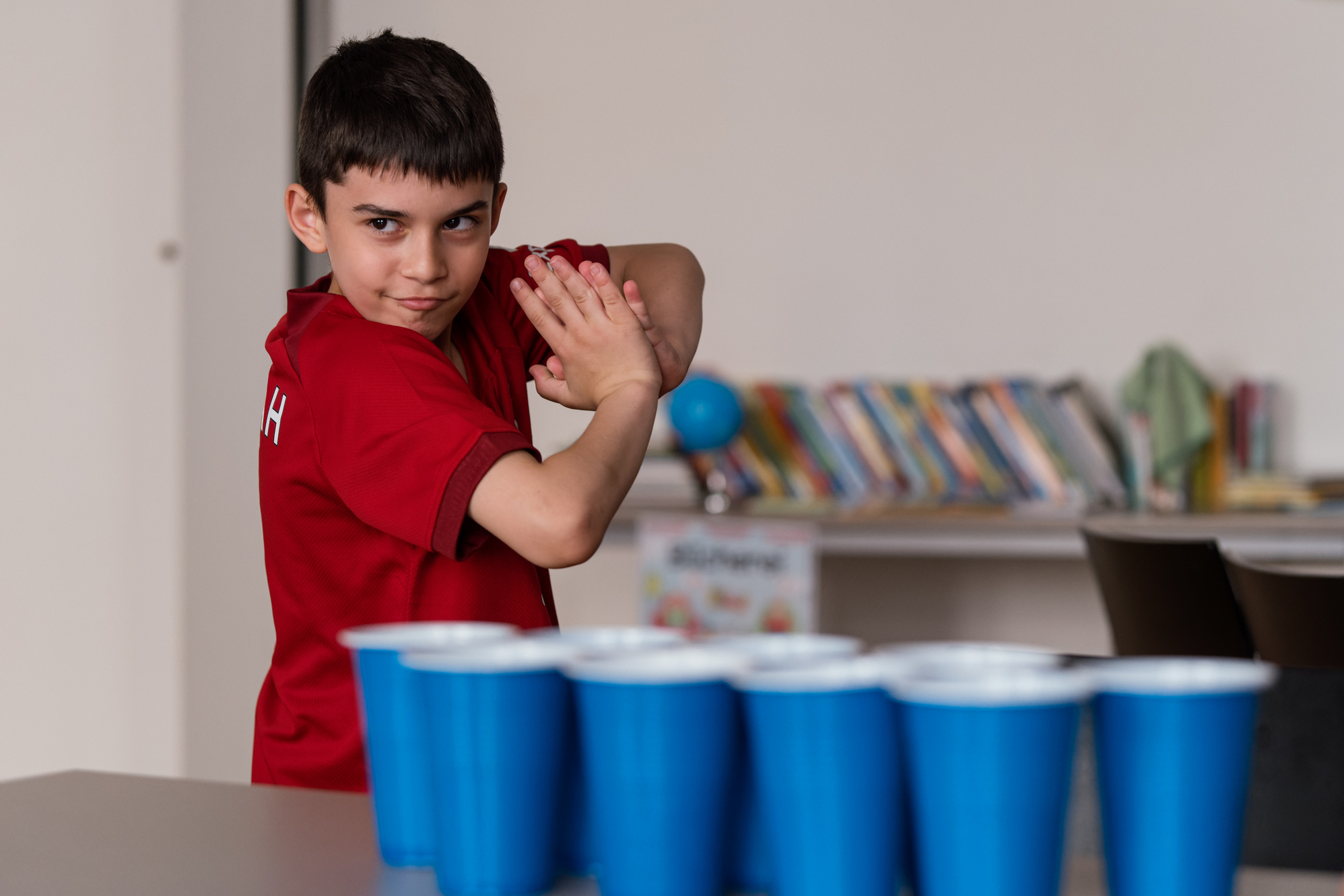 Aufnahme eines Jungen, der eine Siegerpose vor mehreren blauen Bechern auf einem Tisch einnimmt