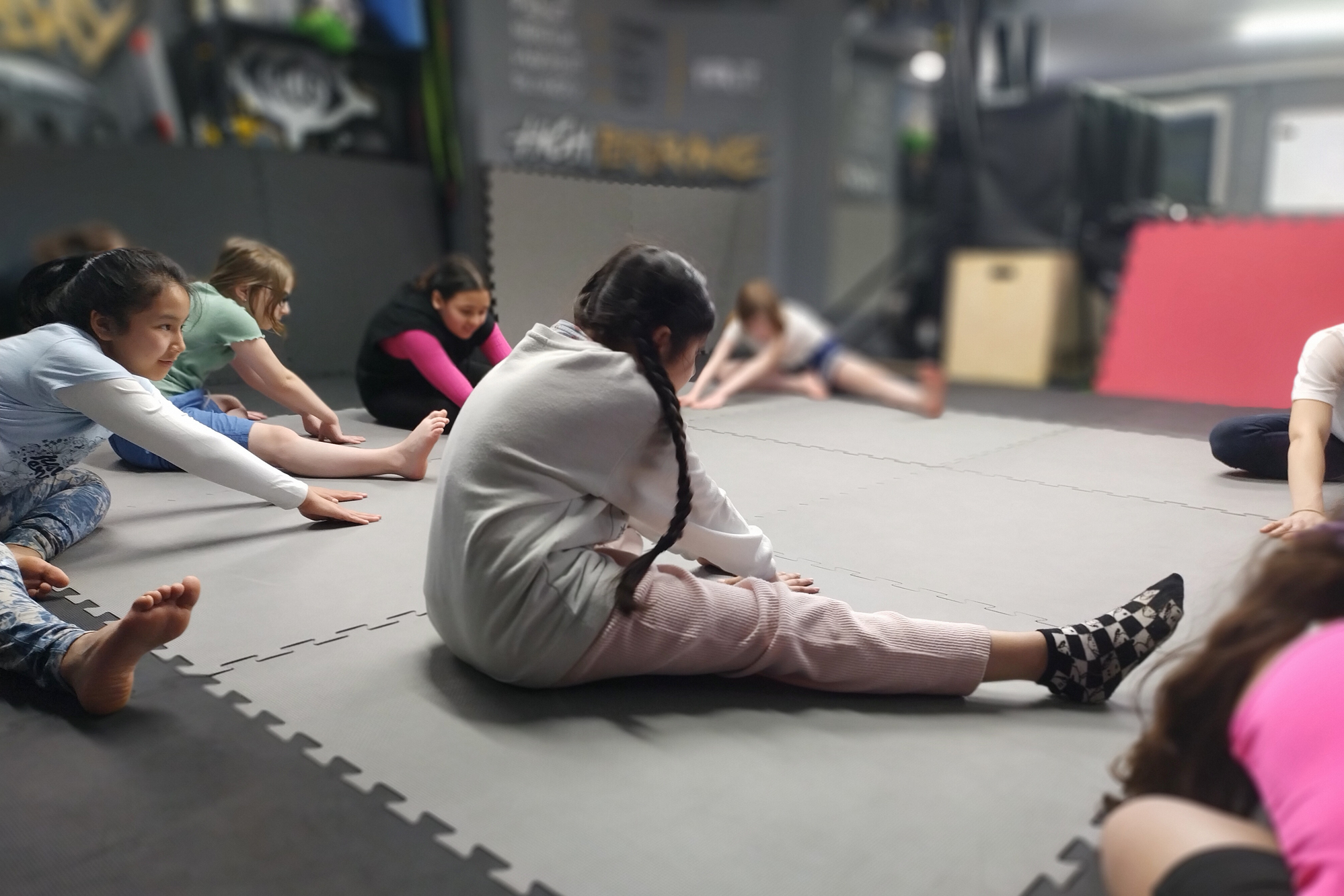 Kinder sitzen auf Turnmatten und machen verschiedene Übungen, sind von hinten fotografiert