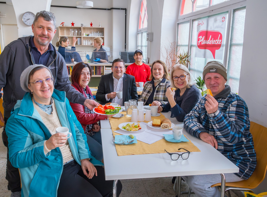 Gruppe von Menschen an einem Tisch, gemeinsam Essen und Getränke genießen.