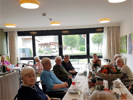 Eine Gruppe älterer Menschen sitzt an einem Tisch in einem hellen Raum.
