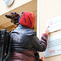 Obdachlose mit Hund auf der Schulter steht vor Haus Sama Türe