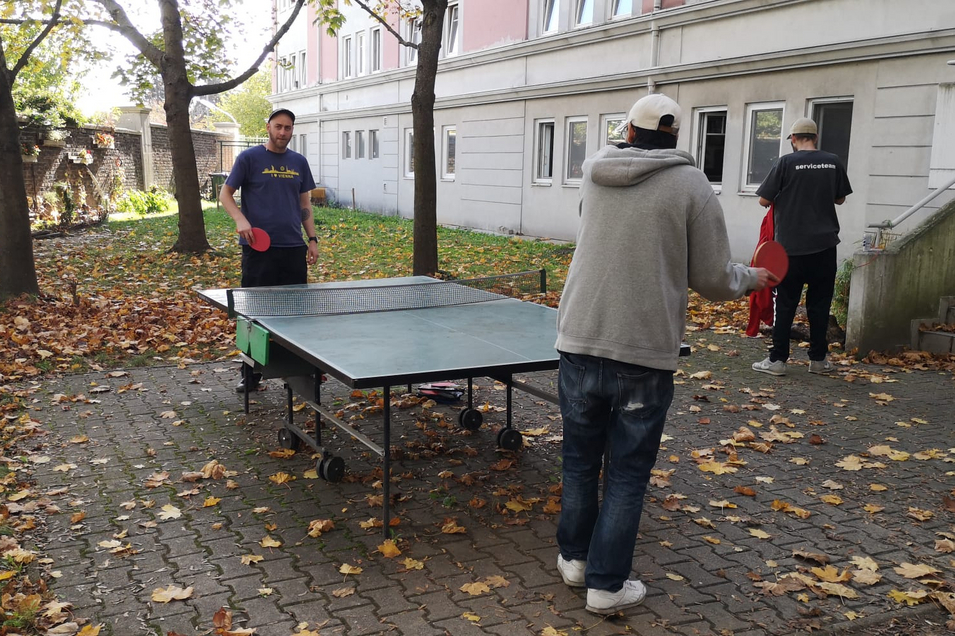 Zwei Bewohner einer Wohnungsloseneinrichtung spielen Tischtennis im Garten