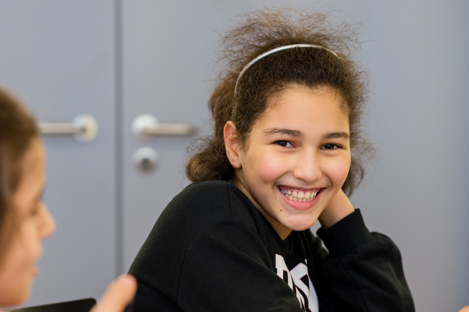 LernLEO - Mädchen mit lockigen Haaren stützt sich auf ihrer Hand ab und lächelt
