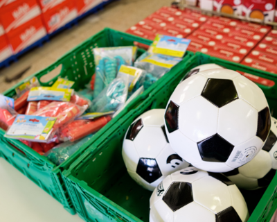 Nahaufnahme Fußbälle für Kinder in grüner Box, daneben anderes Spielzeug abgepackt