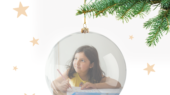 Ein Mädchen mit Buntstiften, das in einer Weihnachtskugel zeichnet.