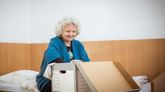 Mobile Wohnbetreuung - Frau packt Karton aus auf Bett