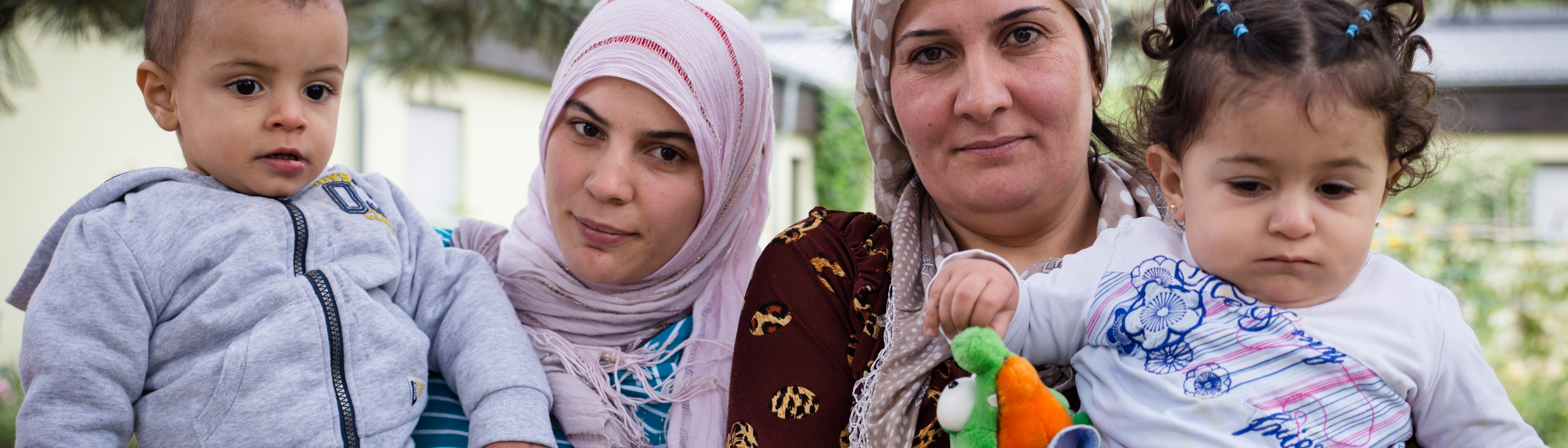 Zwei mit Kopftuch bedeckte Frauen halten jeweils ein Kind am Arm