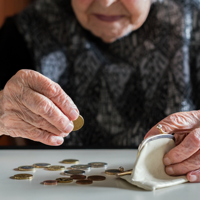 Nahaufnahme ältere Frau die nur bis zum Kinn sichtbar ist, sitzt an Tisch und zählt Geld, hält in der einen Hand Münzen in der anderen alte Geldbörse, einige Münzen liegen auch auf Tisch