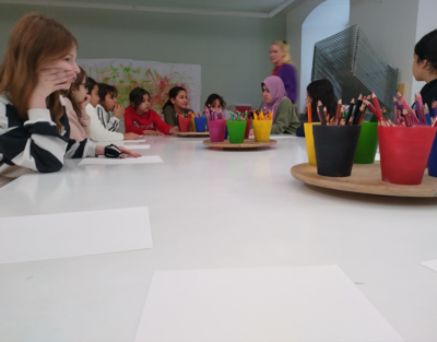 Einige Kinder sitzen an einem Tisch, auf dem Malmaterial vorbereitet ist.