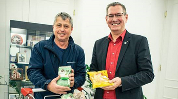 Leiter Sozialmärkte und Bezirksvorsteher Floridsdorf vor vollbefüllten Einkaufswagerl, darauf ein Schild mit Spruch Kaufs ein gibs rein.