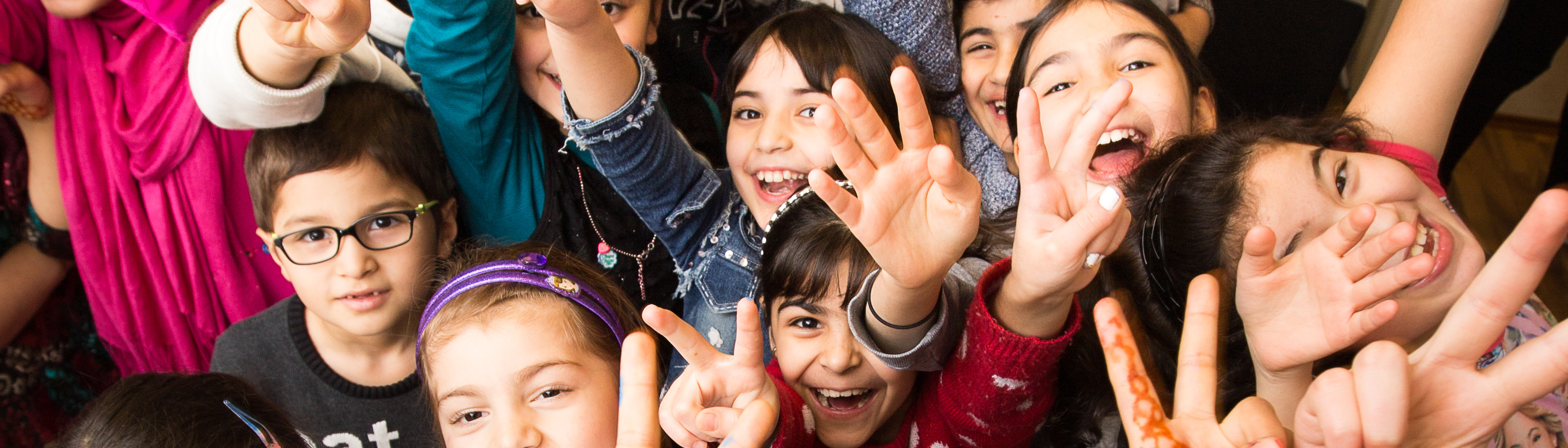 LernLEO - Gruppenaufnahme von ca. 15 Kindern, die Arme in der Luft haben und lachen