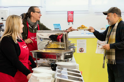 Freiwillige Suppentopf-Mitarbeiter geben Essen an einen Mann aus