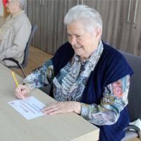 Ältere Frau schreibt an einem Tisch mit einem Stift.