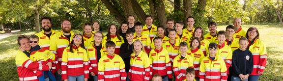 Mehrere Kinder und Betreuer der Samariterjungen stehen vor einem Baum in der Uniformjacke im Park und machen ein Gruppenfoto