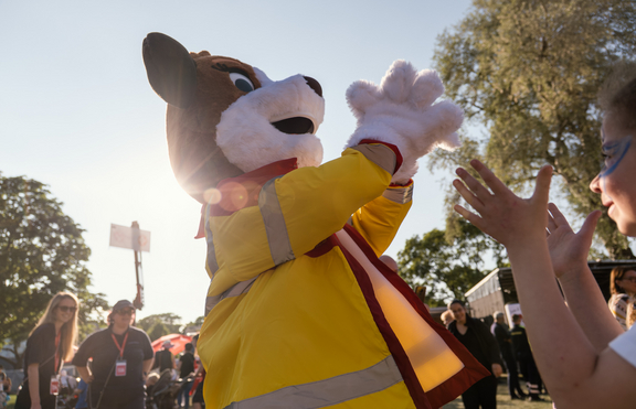 Maskottchen Sam auf Kaiserwiese im Prater, Bild von unten fotografiert, Sam klatscht in die Hände, im rechten unteren Teil des Bildes Kinderhände, im Hintergrund weitere Menschen